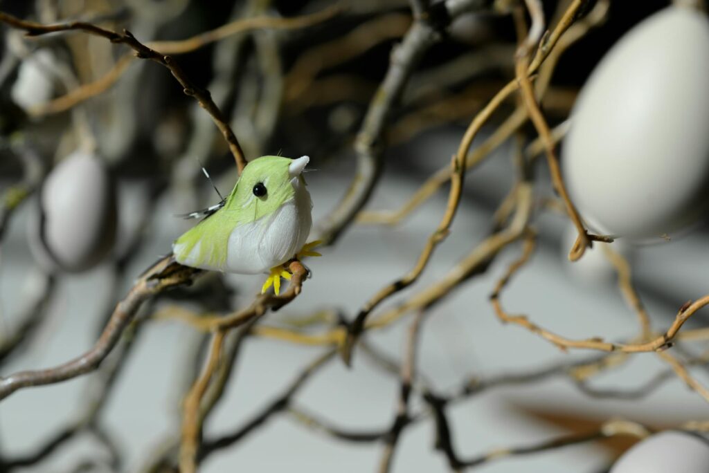 green and white bird toy perched on tree branch at daytime